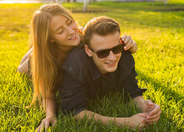 young couple having fun and playing in grass. woman lying over her lover, smiling - Фото, изображение