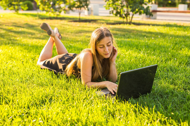 portrait of a beautiful student girl with laptop computer on the green grass in the park in spring or summer time. - Foto, afbeelding