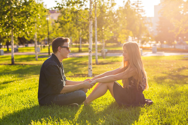 友情、レジャー、夏と人々 のコンセプト - 公園の芝生の上に座っている若い愛のカップル - 写真・画像