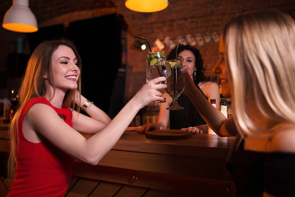 Two pretty Caucasian girls toasting drinking cocktails in pub celebrating birthday - Photo, Image