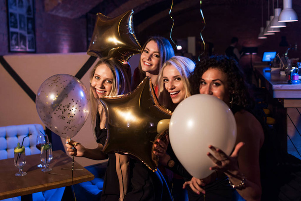 Czterech pięknych młodych kobiet rasy kaukaskiej gospodarstwa balony o wieczór razem w modnym barze - Zdjęcie, obraz