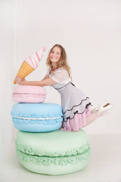 hübsche junge Dame in gepunktetem Pin-up-Kleid mit riesigen Süßigkeiten im weißen Hintergrund Studio - Foto, Bild