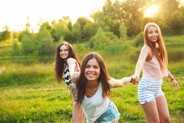 three beautiful girls walking and laughing on sunset in the park. Friendship concept. - Фото, зображення