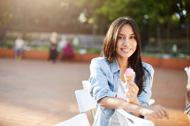 Girl eating icecream in park on a sunny summer day smiling looking at camera enjoying the taste. - Zdjęcie, obraz