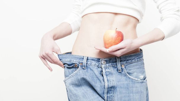 hmotnost ztráta žena drží své staré džíny a apple izolovaných na bílém pozadí - Fotografie, Obrázek