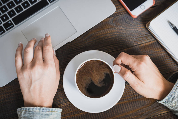 Geschäftsfrau am Morgen. Laptop, Telefon und eine Tasse Kaffee in weiblichen Händen. horizontaler Rahmen - Foto, Bild