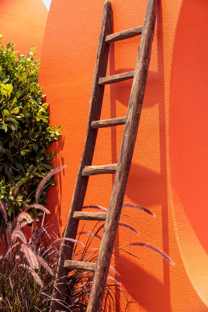 Ρουστίκ ξύλινη σκάλα σε ένα φωτεινό πορτοκαλί τοίχο - Φωτογραφία, εικόνα