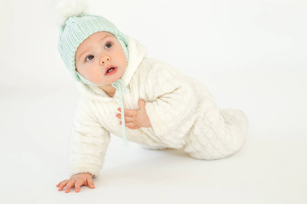 Little baby wearing hat sitting on floor over white background. - Foto, afbeelding