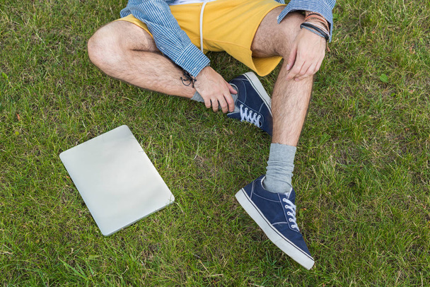 Человек с ноутбуком сидит на траве
 - Фото, изображение
