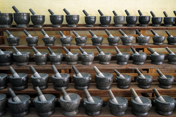 Ensembles de mortier enduit et pilon en pierre de granit de couleur grise et noire disposés sur une étagère en bois à vendre sur le marché local
 - Photo, image