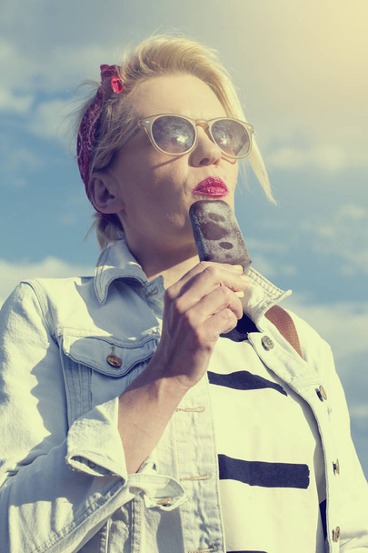 Beautiful blonde with red lips eating chocolate ice cream outdoors - Photo, image