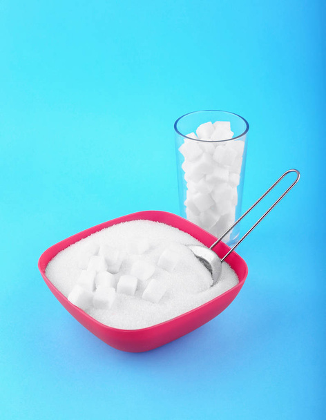 Lasi täynnä sokerikuutioita ja laatikko makea sokeri kirkkaan sininen tausta. Diabetesruokavalioon liittyvät terveysriskit. Epäterveellinen ruokavalio käsite
.  - Valokuva, kuva