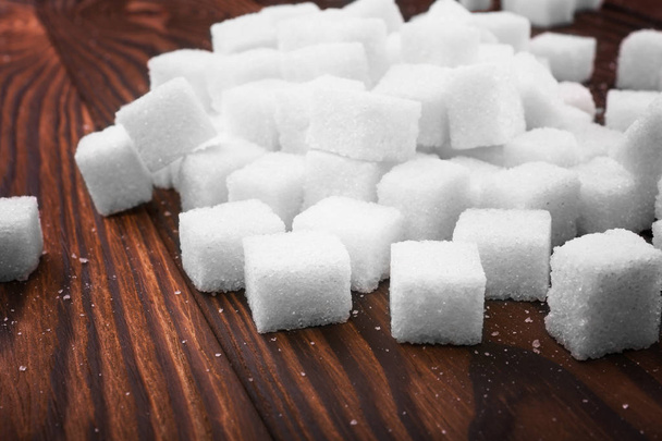 Close-up picture of sugar cubes on a dark brown wooden table. A pile of white pieces of sugar cubes for cooking. The health risks related to diabetes.  - Zdjęcie, obraz