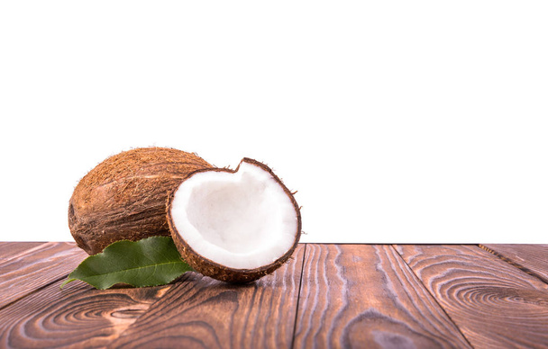 Nahaufnahme hellbraune Kokosnüsse mit grünen Blättern auf einem dunkelbraunen Holztisch, isoliert auf weißem Hintergrund. eine leckere ganze Kokosnuss. leckere tropische Kokosnüsse.  - Foto, Bild
