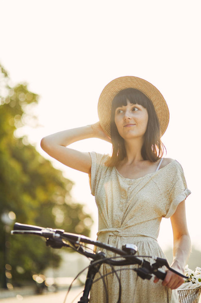 Outdoor Portret van aantrekkelijke jonge brunette in een hoed op een fiets. - Foto, afbeelding