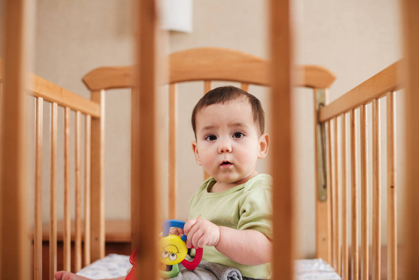 Rozkošný chlapeček sedí v jeho postýlce nebo kolébce - Fotografie, Obrázek
