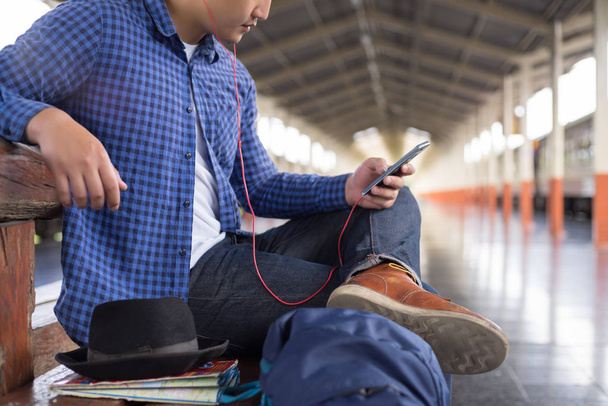 Sırt çantalı bir gezgin tren istasyonunda müzik dinliyor, seyahat konsepti... - Fotoğraf, Görsel