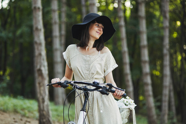 Außenporträt der attraktiven jungen Brünette mit Hut auf einem Fahrrad. - Foto, Bild