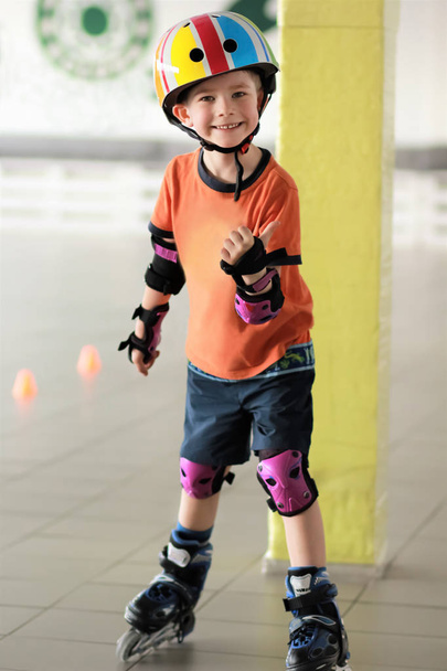 Vijf-jarige jongen met zijn duim omhoog waaruit blijkt dat hij houdt van rolschaatsen. Uitgeruste jongen dragen van een helm. Trainen in een sportschool.  - Foto, afbeelding