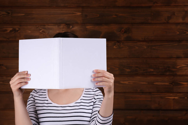 Γυναίκα που κρατά άνοιγμα βιβλίου με κενό εξώφυλλο στο φόντο ξύλινη - Φωτογραφία, εικόνα
