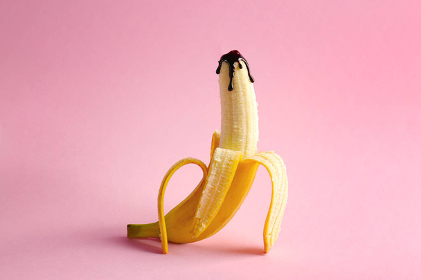 Banana covered with chocolate sauce on color background. Sex concept - Foto, imagen