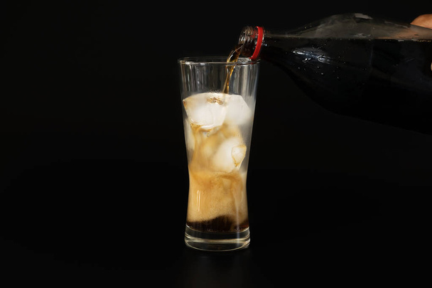 Giet de cola uit een plastic fles in een glazen van ijs  - Foto, afbeelding