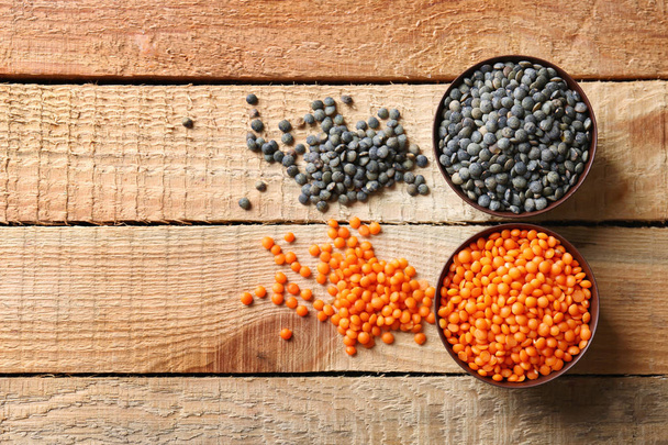 Two bowls of red and black lentils on wooden background - Фото, изображение