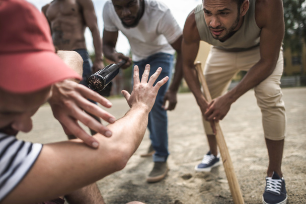 hombres atacando a otro con bates de béisbol
 - Foto, Imagen