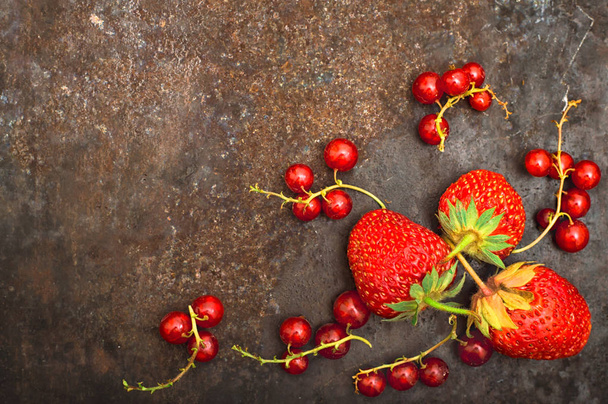 Fresh red currant and strawberry with mint. On a old black background. Top view. Close-up - 写真・画像