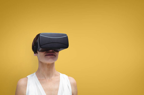 Woman in VR headset standing against yellow background - Фото, изображение