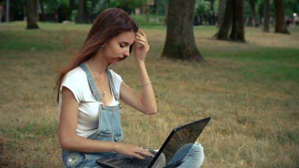 cute young girl keeps on legs laptop and sits on the lawn - Séquence, vidéo
