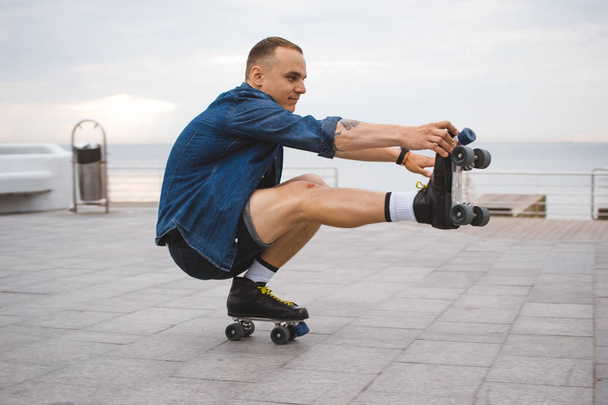 Young caucasian man roller skating with quad skates near the sea - 写真・画像