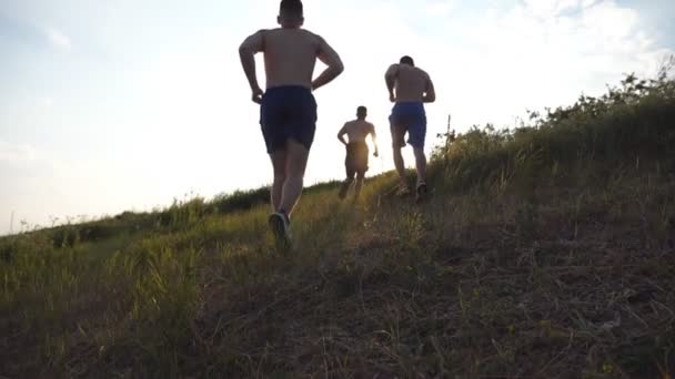 Un gruppo di giovani che corre sulla collina verde sopra il cielo blu con un bagliore solare sullo sfondo. Gli atleti di sesso maschile fanno jogging nella natura al tramonto. Corridori sportivi che salgono all'alba all'aperto. Rallentatore
 - Filmati, video