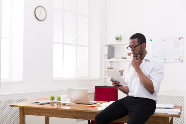 Συλλογισμένος μαύρο επιχειρηματίας στο σύγχρονο γραφείο, εργασία με tablet - Φωτογραφία, εικόνα