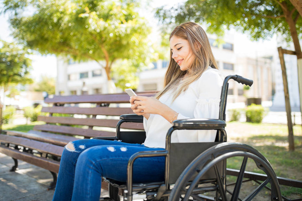 Woman in wheelchair with a smartphone - Фото, изображение