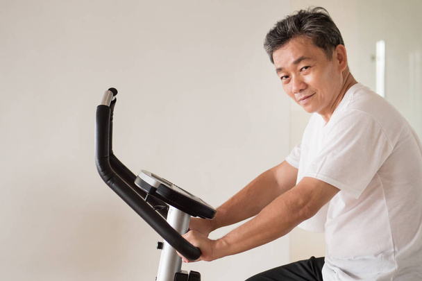 senior grijsaard fietsen, trainen, trainen in de fitnessruimte met modus - Foto, afbeelding