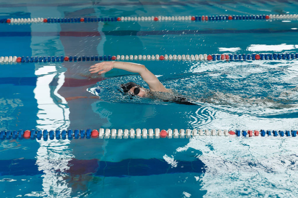 Mladá dívka v brýle a čepici plavání styl tahu procházení v modré vodě bazénu. - Fotografie, Obrázek
