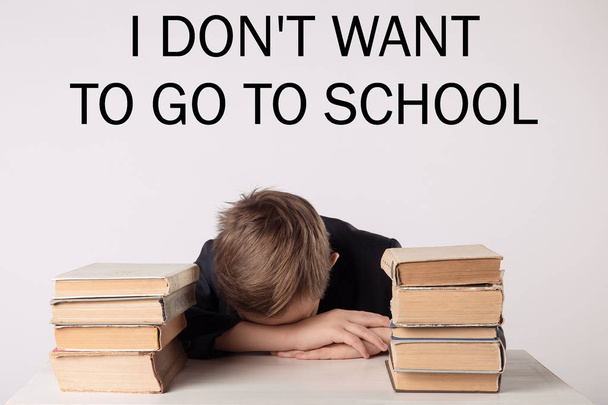 Alumno de traje en su escritorio sobre fondo gris con libros. El chico se durmió durante la tarea. Inscripción 'No quiero ir a la escuela'
. - Foto, Imagen