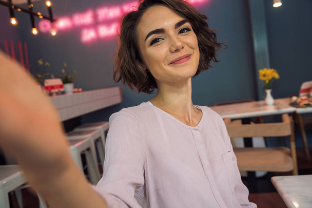 Smiling pretty girl taking a selfie in a cafe - Фото, зображення