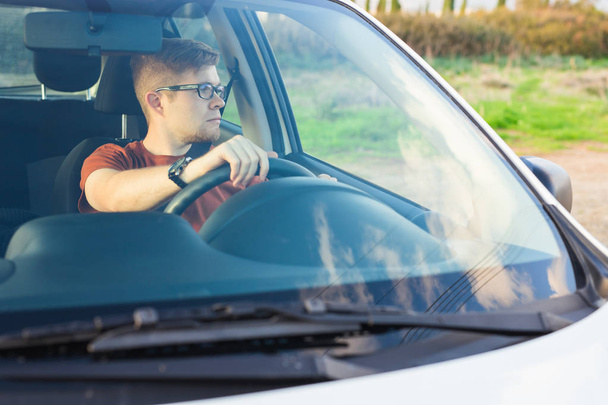 glücklicher Besitzer. schöner junger Mann sitzt entspannt in seinem neu gekauften Auto und schaut aus dem Fenster - Foto, Bild