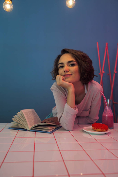 Jovencita feliz sentada a la mesa con un libro
 - Foto, Imagen
