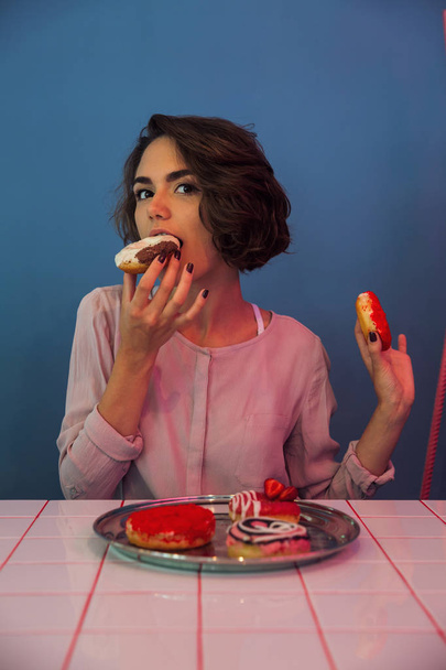 Muchacha hambrienta comiendo rosquillas en la mesa
 - Foto, imagen