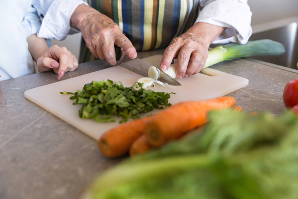 Close up of a senior lady cutting vegetables on a board - Foto, afbeelding