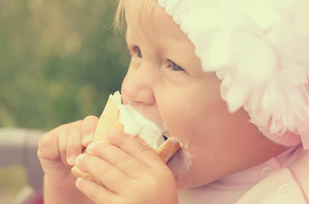 ein kleines Mädchen isst Eis und verschmiert ihr Gesicht. - Foto, Bild