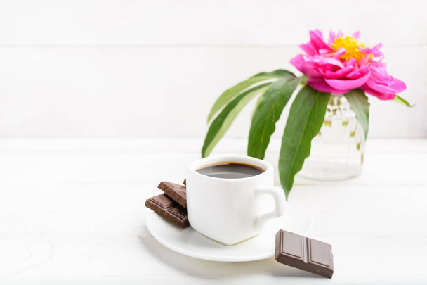 White cup of coffee with flower in vase and chocolate on white wooden background - Foto, immagini