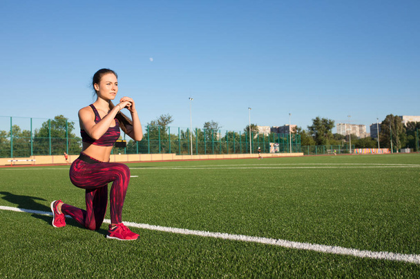 Young happy sportswoman in sportswear making lunges exercise on stadium field area outdoors. Healthy lifestyle concept, sport activity. - Foto, Imagen