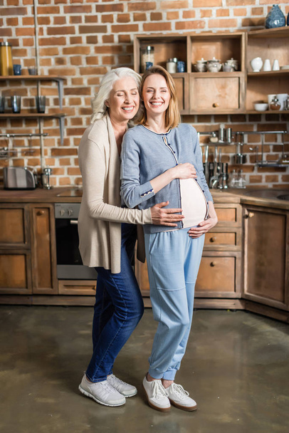 raskaana oleva nainen ja hänen äitinsä keittiössä
 - Valokuva, kuva