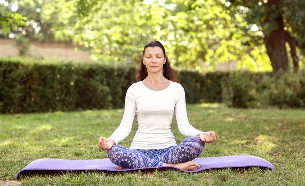 Pretty woman doing yoga in morning park. Lotus asana. Healthy lifestyle outdoor conception. Sport. Woman nature portrait doing exercises. Healthy lifestyle. - Фото, изображение