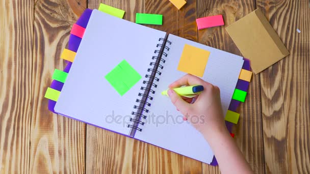 Woman opens notepad and draws smile. Open notepad with office supplies. Open notepad lies on a wooden desktop with marker, pencil, pen and Stickers - Footage, Video
