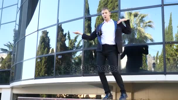 A young happy businessman in a business suit dancing modern ballet and wacking against the backdrop of a business center building. Slow-mo - Filmagem, Vídeo